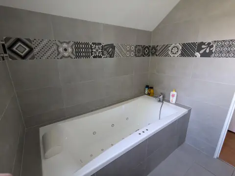 Baignoire balnéo à buses, tablier carrelé gris et frise de carreaux à motifs noir et blanc, sous pente