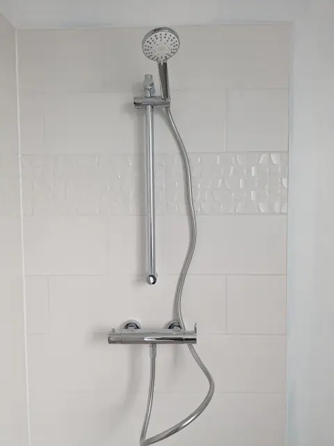 Colonne de douche chromée avec mitigeur thermostatique, barre et douchette, sur carrelage blanc
