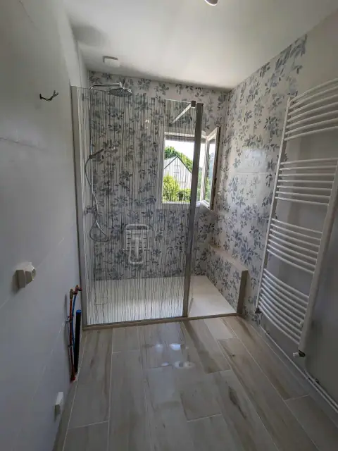 Salle de bains avec douche à paroi vitrée, carrelage mural à motif floral bleu et grand sèche-serviettes blanc