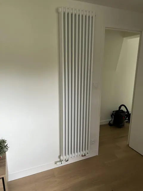 Radiateur vertical blanc à colonnes, posé dans une pièce aux murs blancs et au parquet clair