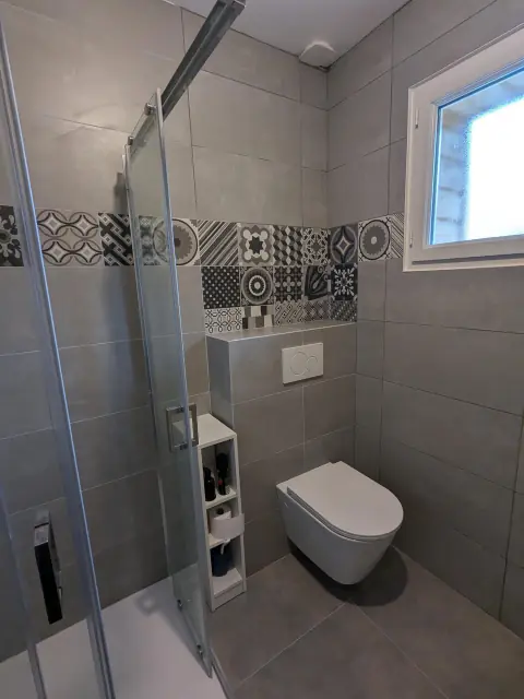 WC suspendu sur bâti carrelé gris, frise de carreaux de ciment noir et blanc, douche à paroi coulissante